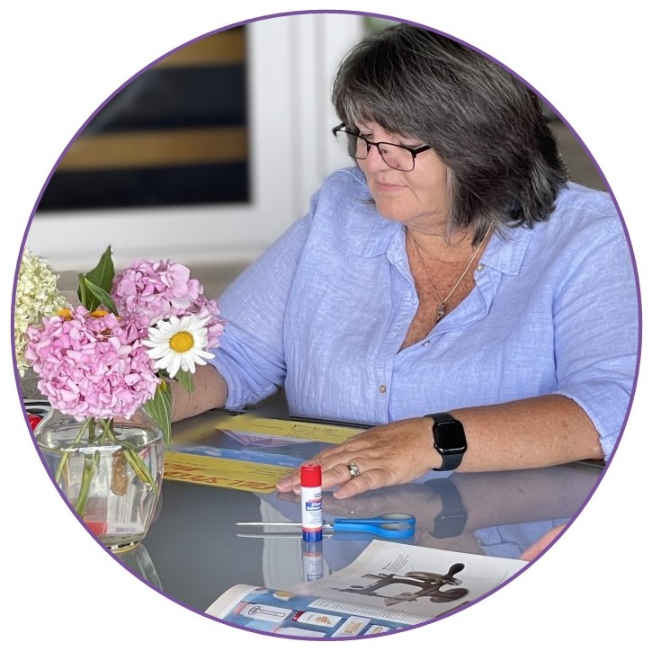 A woman is creating a poster at a table with scissors, glue and magazines.