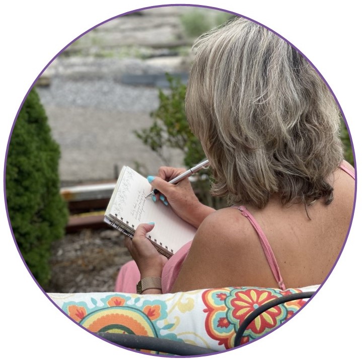 A woman writes in a journal on a bench by the water on The Loss Art property