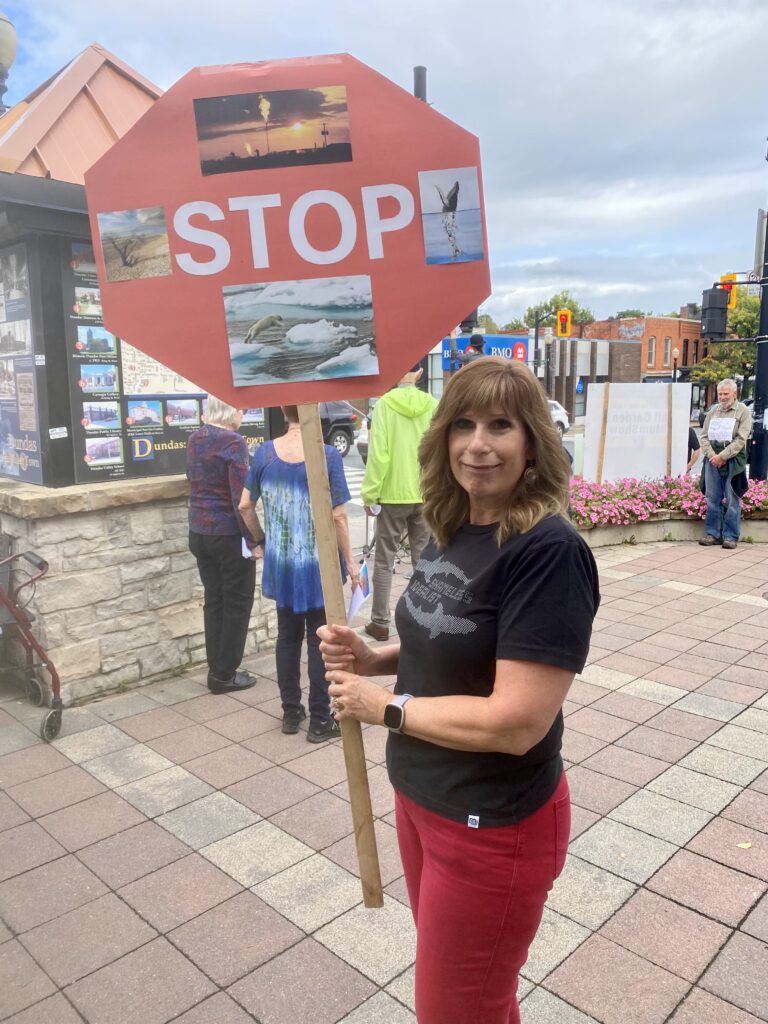 Julie is carrying a sign saying "Stop" with images of climate destruction like burning fossil fuel and a field dead from draught.